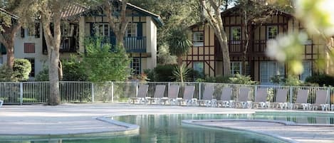 Un área de piscina con sillas de descanso y un edificio con balcón al fondo.