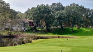 A golf course with a pond, trees, and a building with a red balcony. - Villa ALICE ideally located in the heart of the MOLIETS-ET-MAA golf course (MOLIETS-ET-MAA)