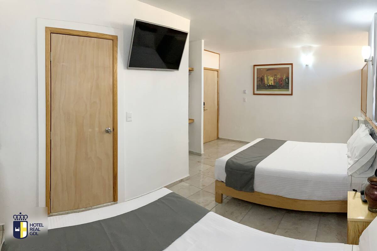 A hotel room with a bed, a television mounted on the wall, a painting, and a window with curtains.