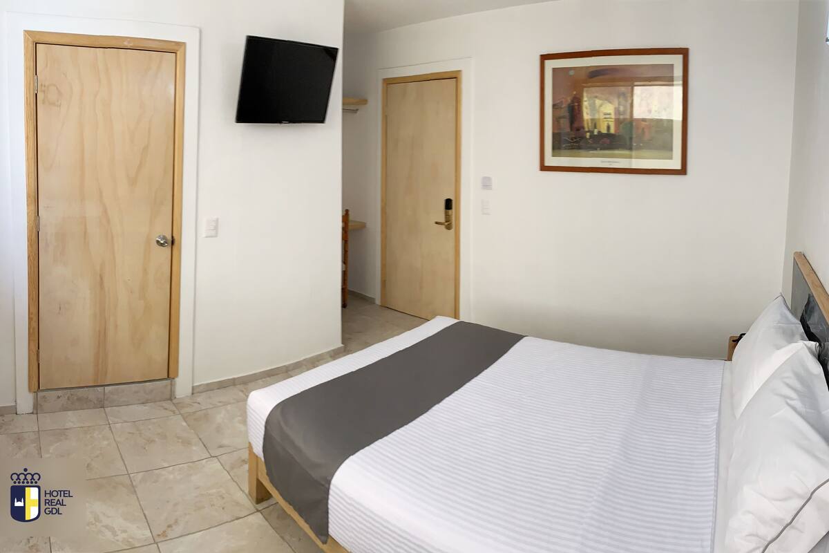 A hotel room with a bed, a television, a framed picture, and wooden doors.