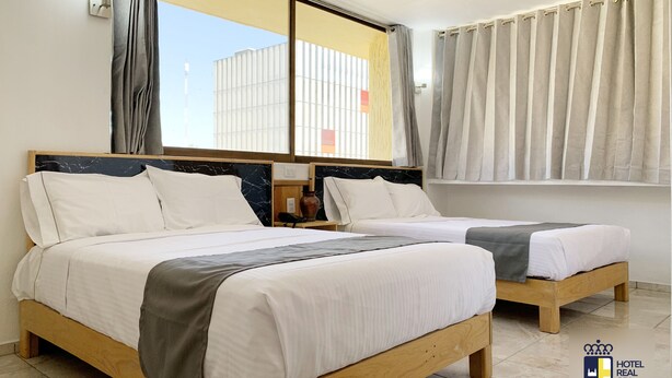 Two wooden beds with white bedding, a nightstand with a lamp, and a window with curtains. - Hotel Real GDL (Guadalajara)