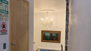 A hallway with a wooden door, a chandelier, a framed painting, and a staircase leading to another room. - Hotel Real GDL (Guadalajara)