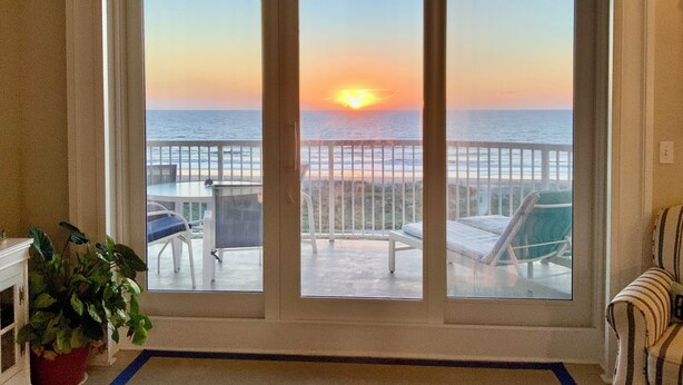 A room with a large sliding glass door leading to a balcony with a view of the sunset over the ocean. - Luxury 5th Floor Oceanfront Condo next to Ritz Carlton! (Fernandina Beach)