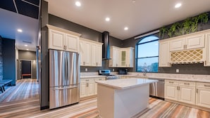 A modern kitchen with a central island, stainless steel appliances, and a view through a large window. - Hotel Lexen Santa Clarita Valencia Near Six Flags (Newhall)