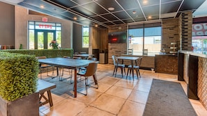 A modern restaurant interior with a brick accent wall, a large window, and a flat-screen TV mounted on the wall. - Hotel Lexen Santa Clarita Valencia Near Six Flags (Newhall)