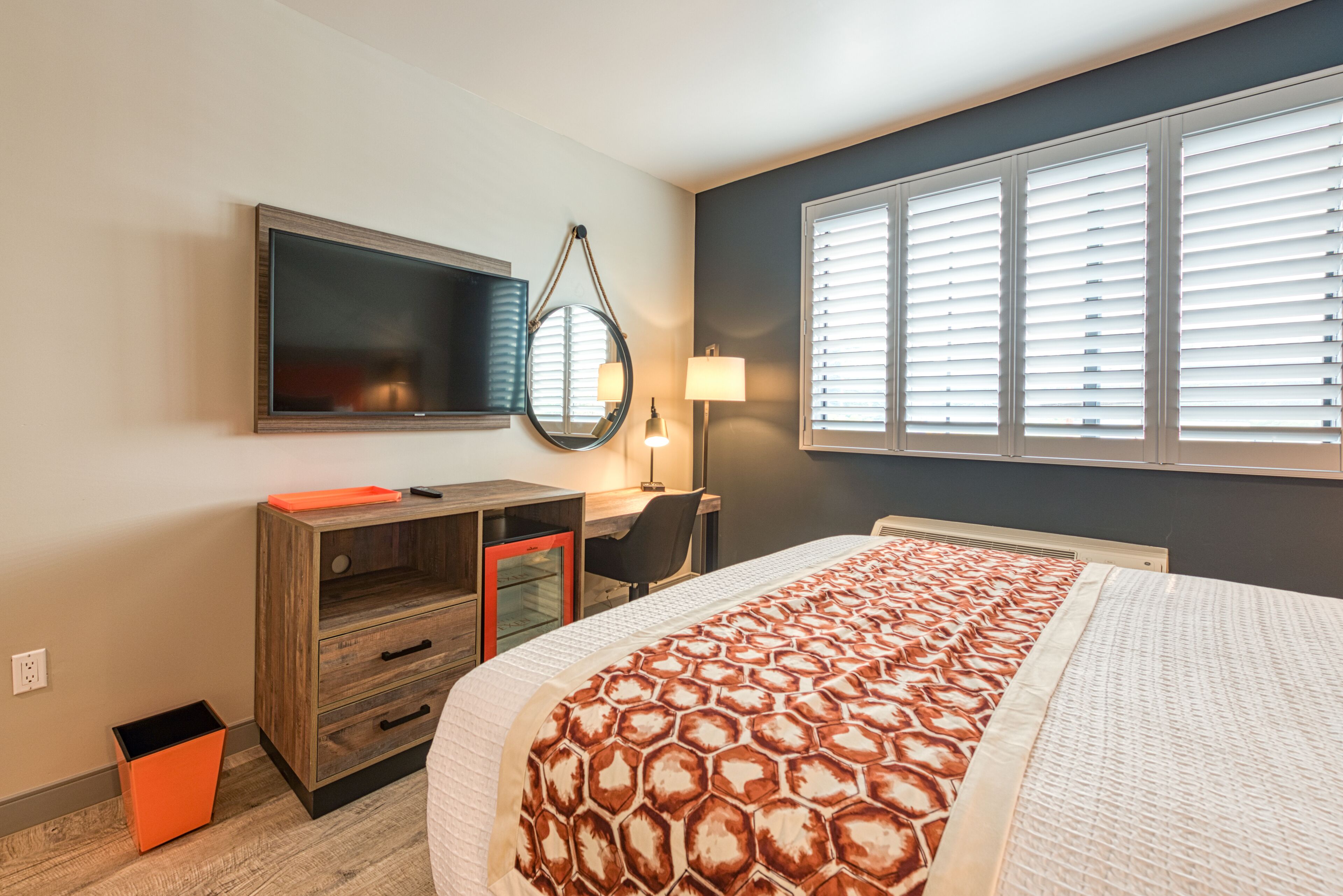 Une chambre d’hôtel équipée d’un lit, d’un bureau, d’une chaise, d’une télévision et d’une fenêtre avec des stores.