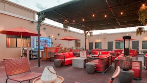 An outdoor seating area with red and brown wicker furniture, a bar, and a sheltered space with string lights. - Hotel Lexen Santa Clarita Valencia Near Six Flags (Newhall)