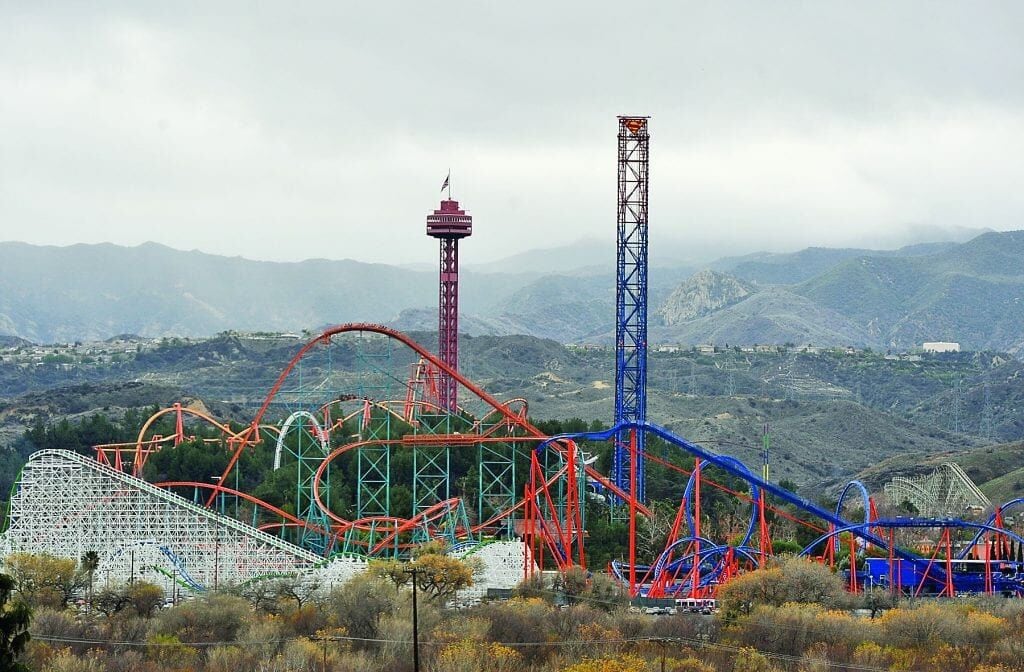 A roller coaster with a red and blue track, a tall tower, and a mountainous backdrop.