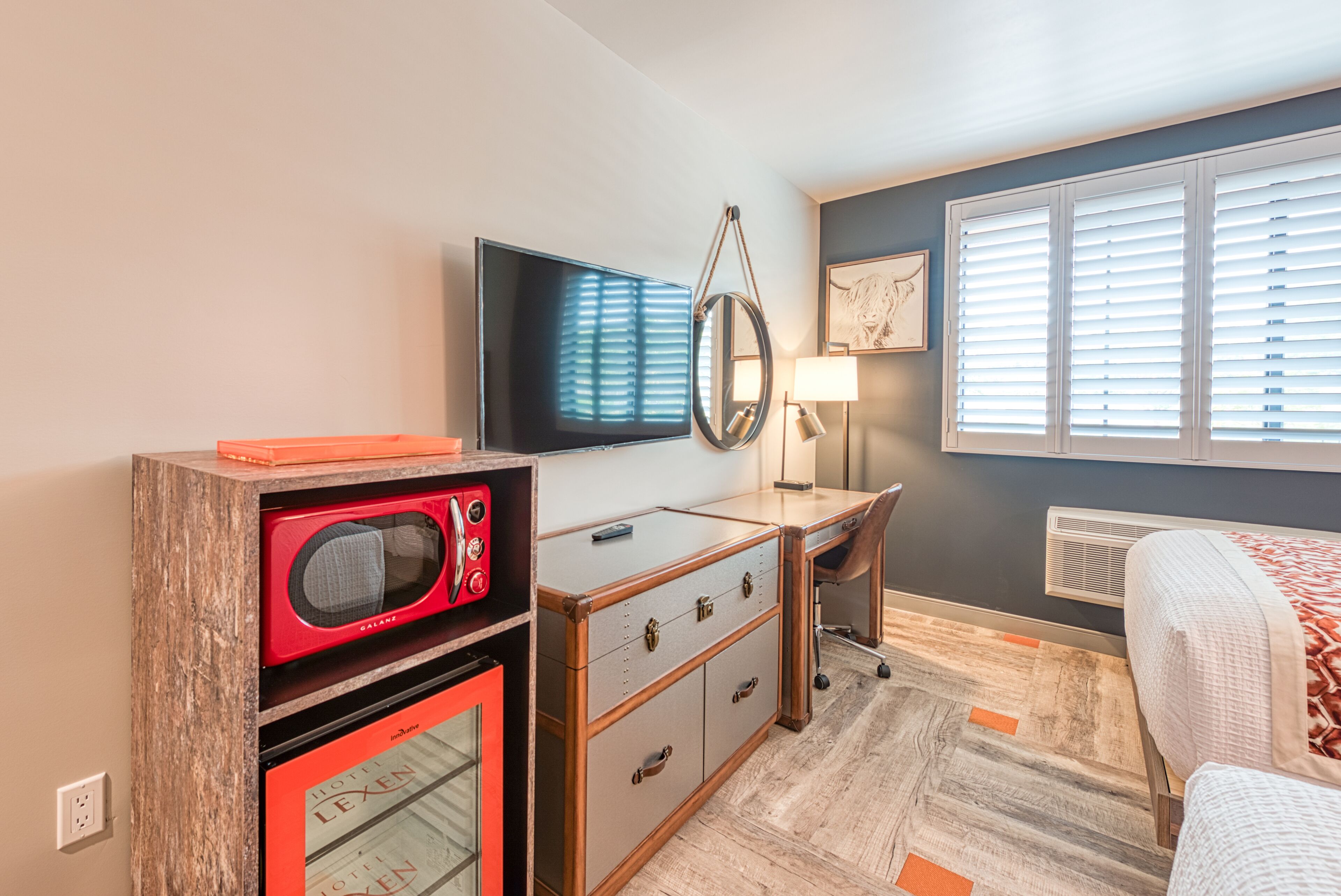 A hotel room with a flat-screen TV, a desk with drawers, a red microwave, and a bed with a patterned blanket.