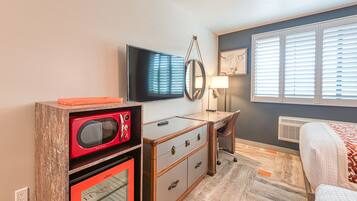 A hotel room with a flat-screen TV, a desk with drawers, a red microwave, and a bed with a patterned blanket.