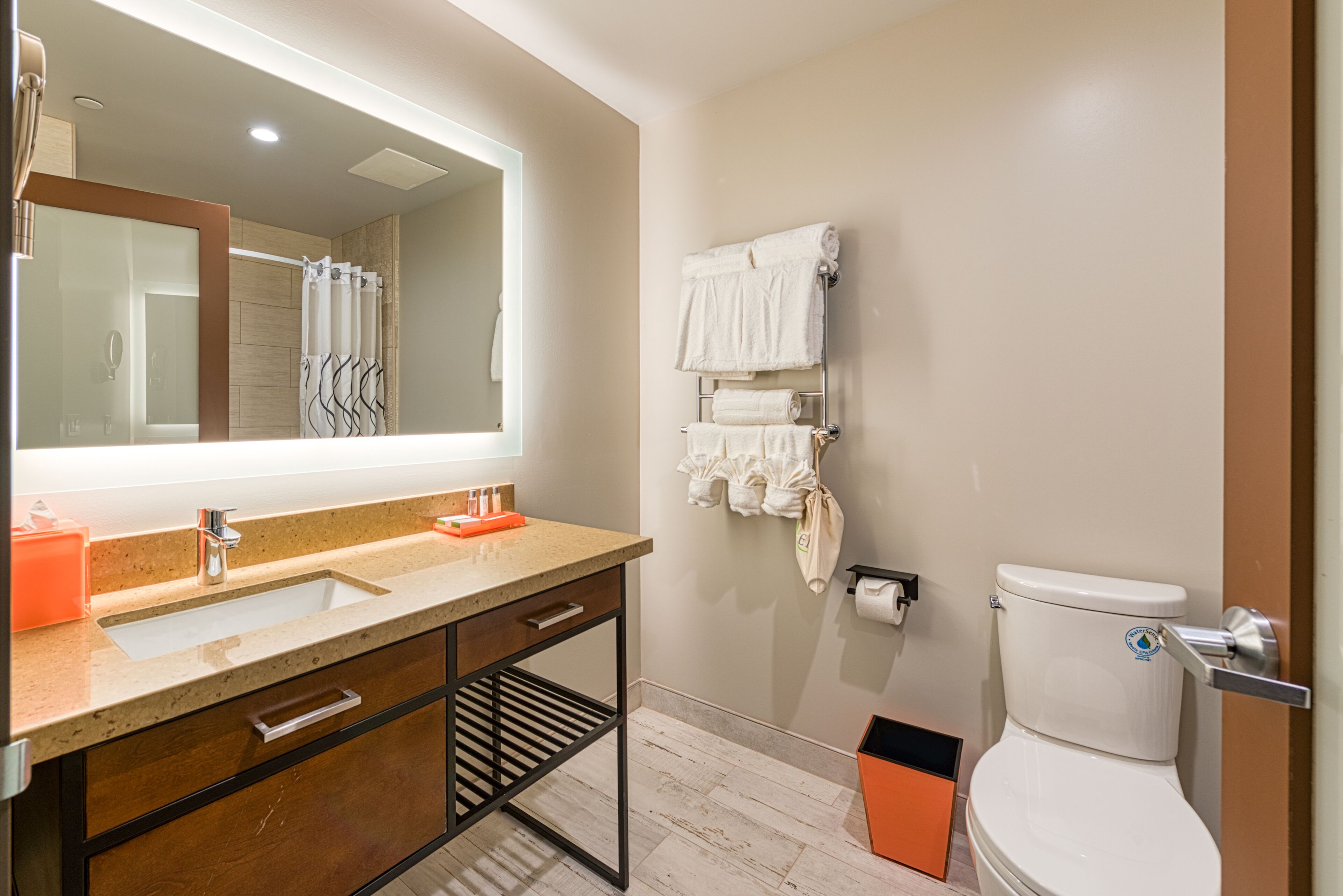 A modern bathroom with a large mirror, a sink, a toilet, and a towel rack.