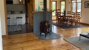 Un amplio salón con una estufa de leña en el centro, una mesa de comedor con sillas y un ventilador de techo.