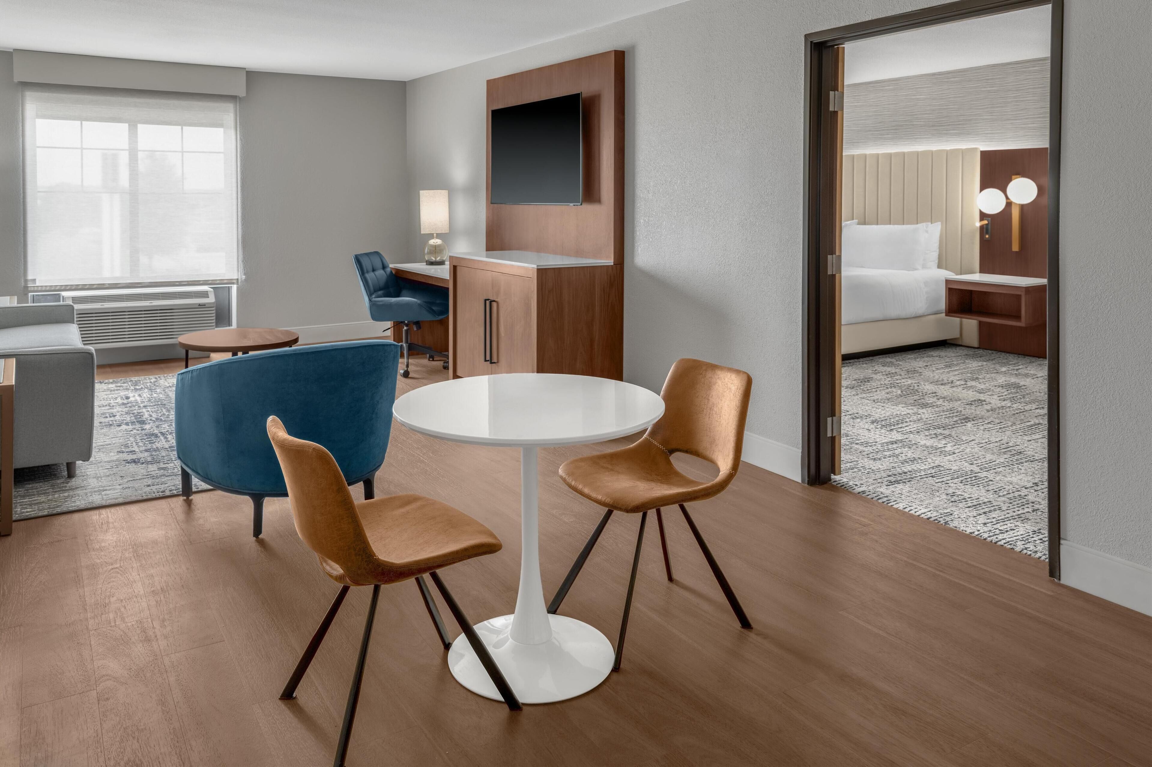 Une chambre d’hôtel avec une table ronde, deux chaises, un téléviseur, un bureau et un lit.