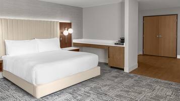 A modern hotel room with a bed, bedside table, built-in desk, and a wardrobe.