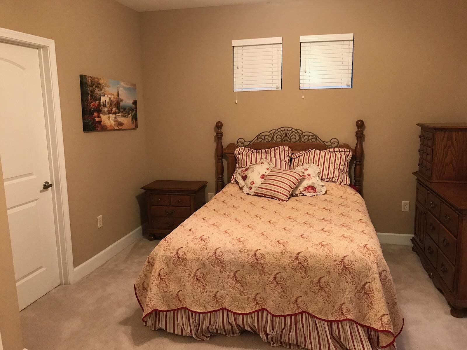 A bedroom with a bed, a nightstand, a dresser, and two windows.