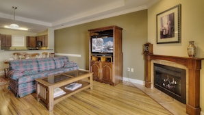 A living room with a plaid sofa, a glass coffee table, a fireplace, and a television. - Lake Life Luxury on the Water (Bean Station)