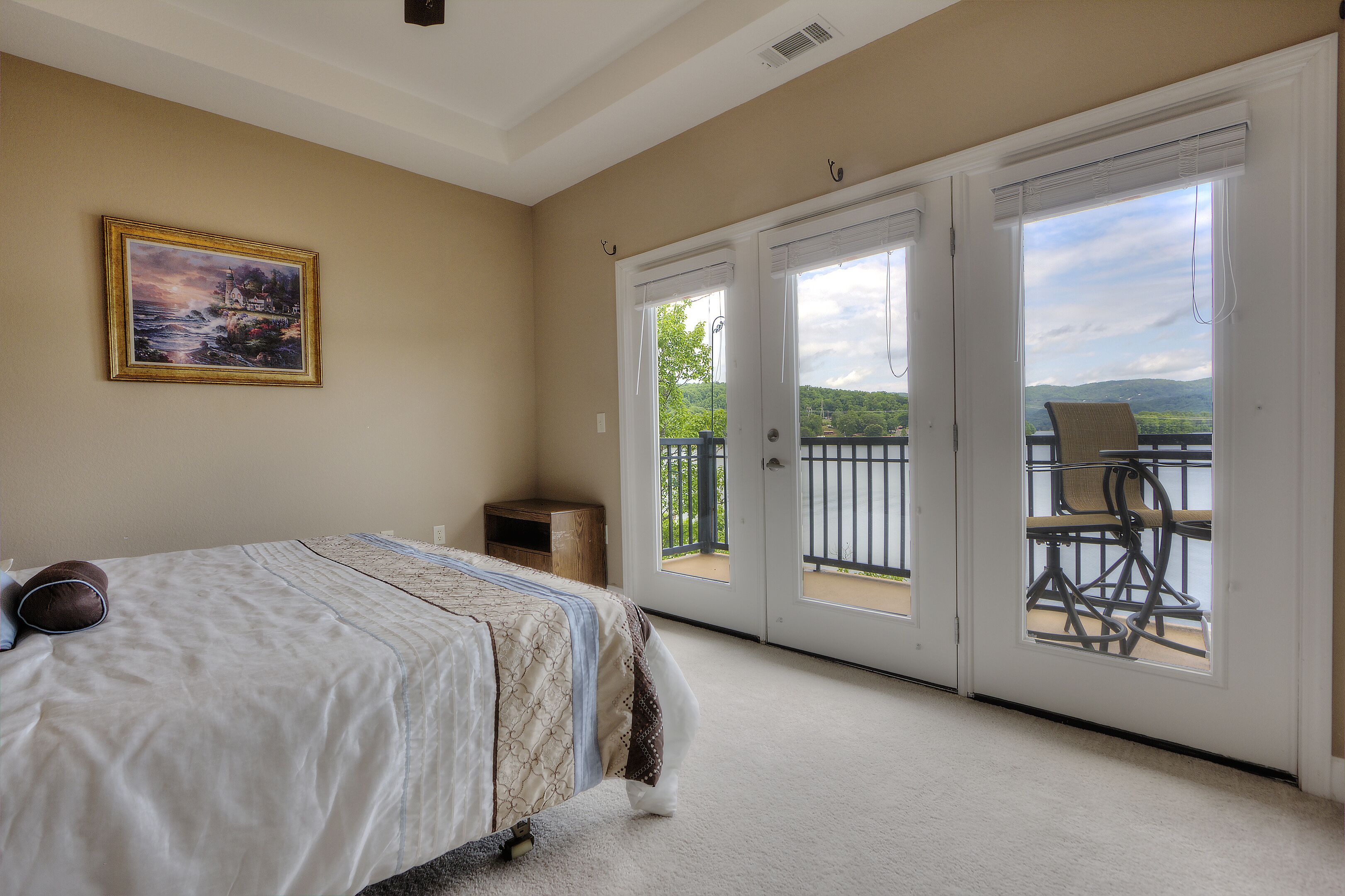 A bedroom with a bed, a painting, and a balcony with a chair and table.
