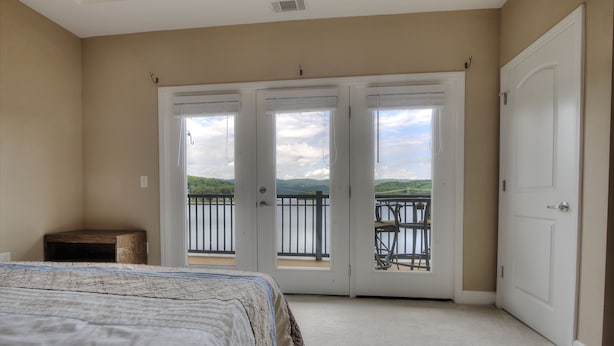 A bedroom with a large bed, a nightstand, and a sliding glass door leading to a balcony with a view of greenery and mountains. - Lake Life Luxury on the Water (Bean Station)