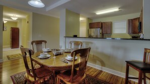 A dining area with a wooden table and chairs, a kitchen in the background, and a hallway leading to another room. - Lake Life Luxury on the Water (Bean Station)