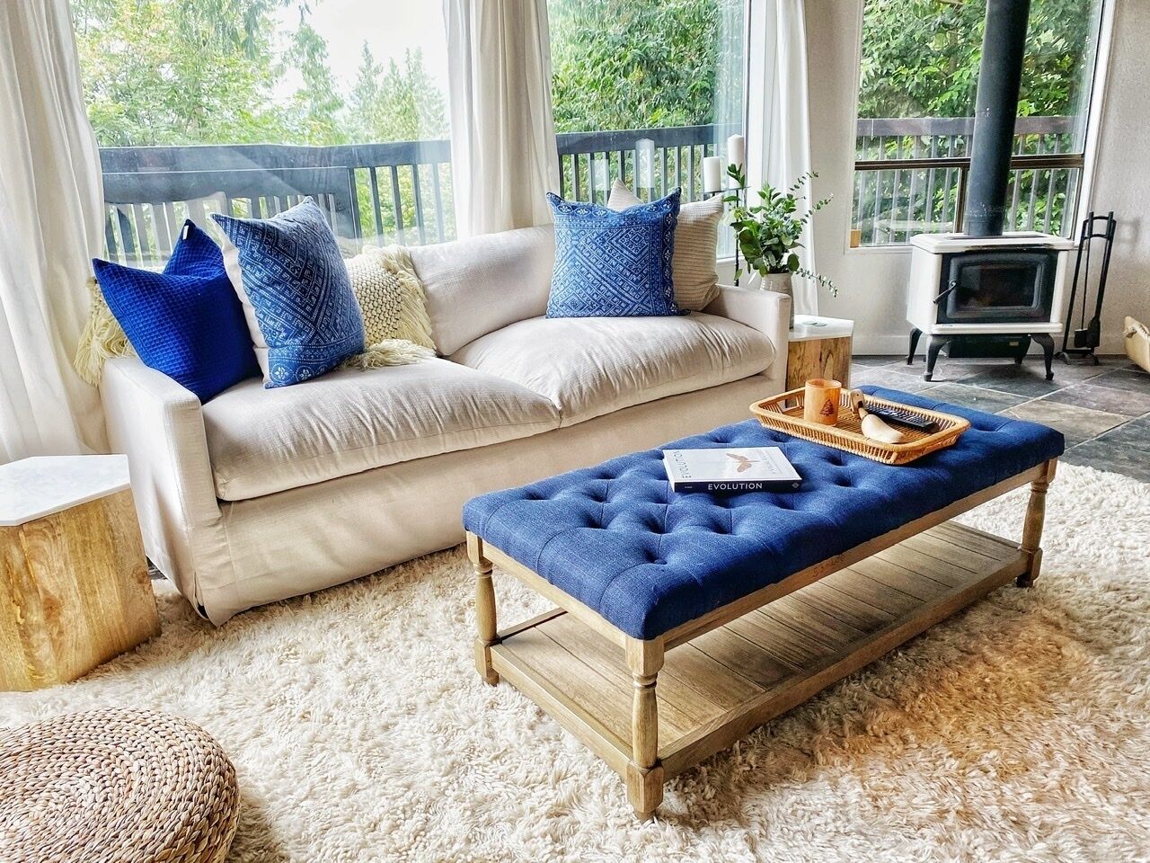 A cozy living room with a sofa, a blue ottoman, and a fireplace.