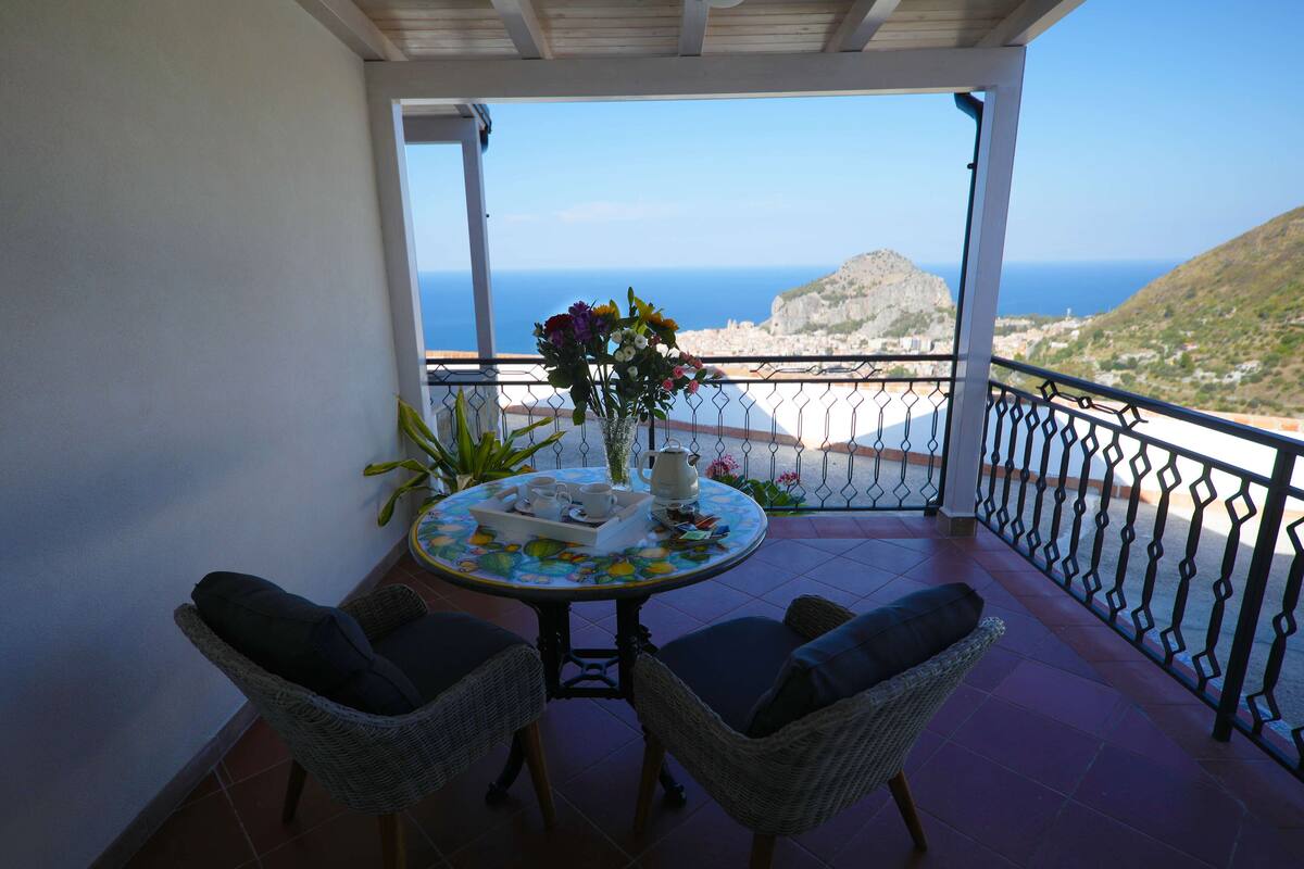 A balcony with wicker chairs, a table with a floral tablecloth, and a vase of flowers.