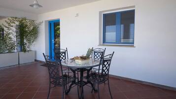 A dining area with a round table and four chairs, a bowl of fruit, and a window with blue trim.