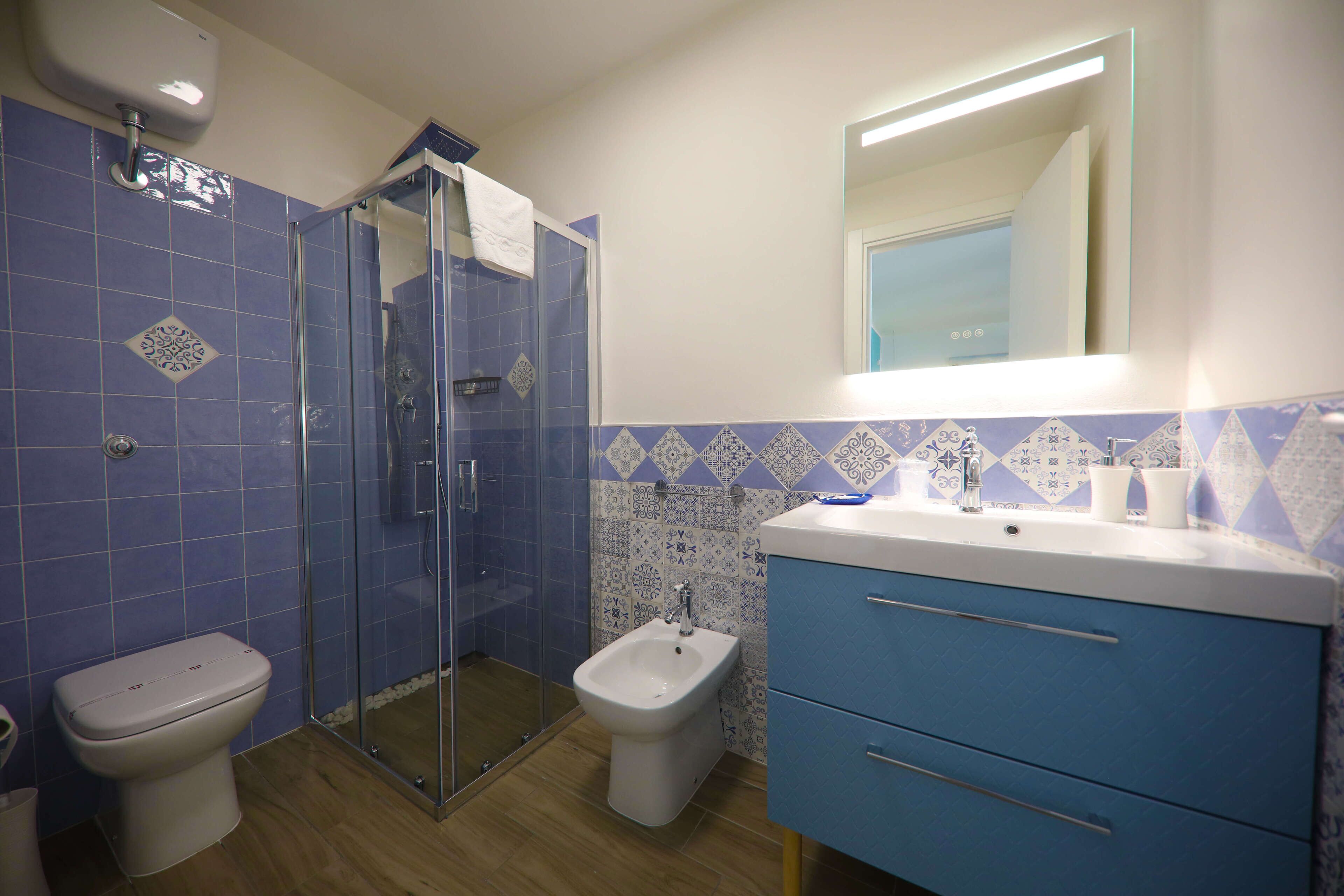 A bathroom with a glass shower enclosure, a bidet, and a sink with a mirror above it.