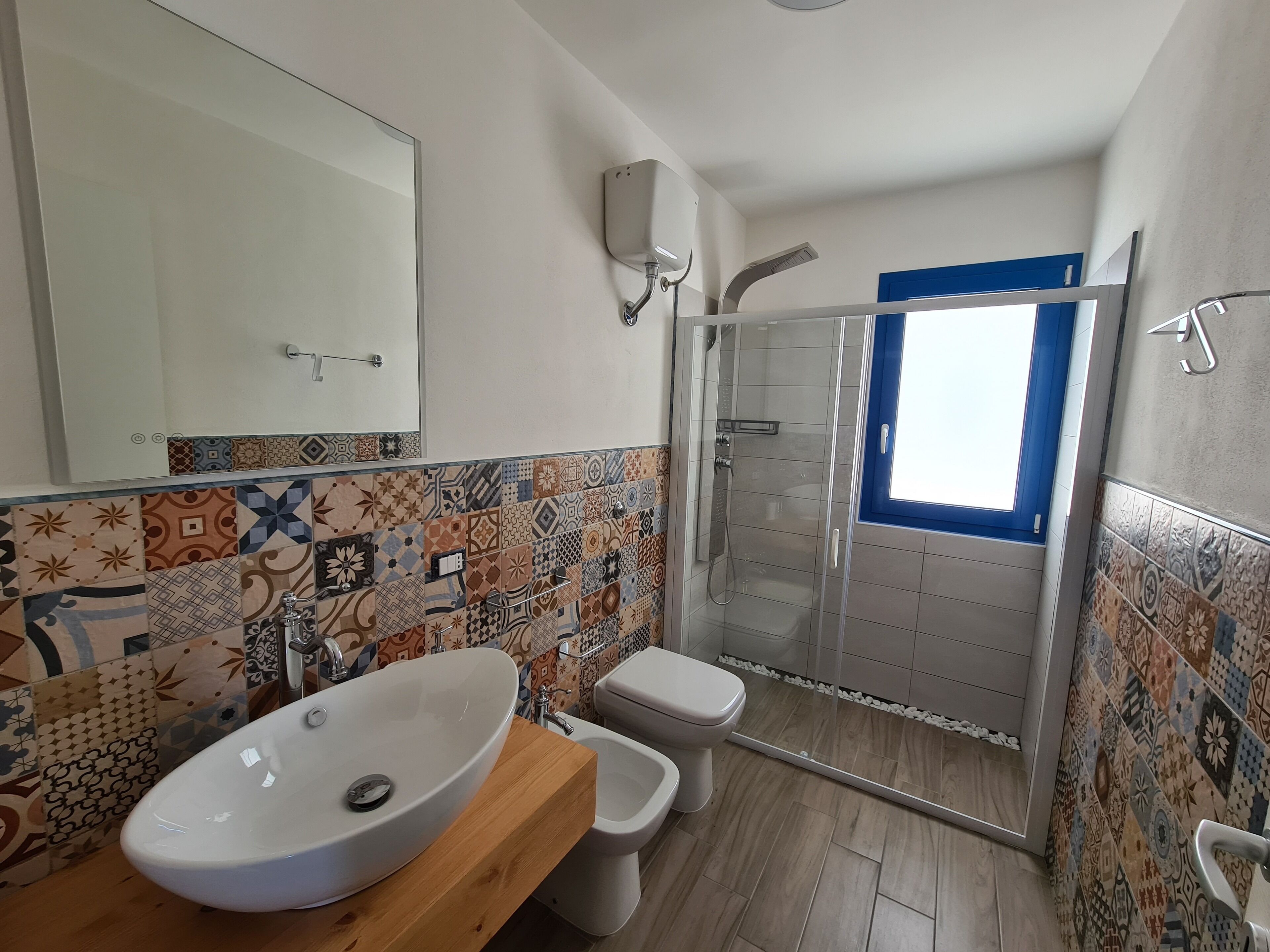 Ein Badezimmer mit gefliestem Spritzschutz, einem weißen Waschbecken, einer Toilette und einer Duschkabine.