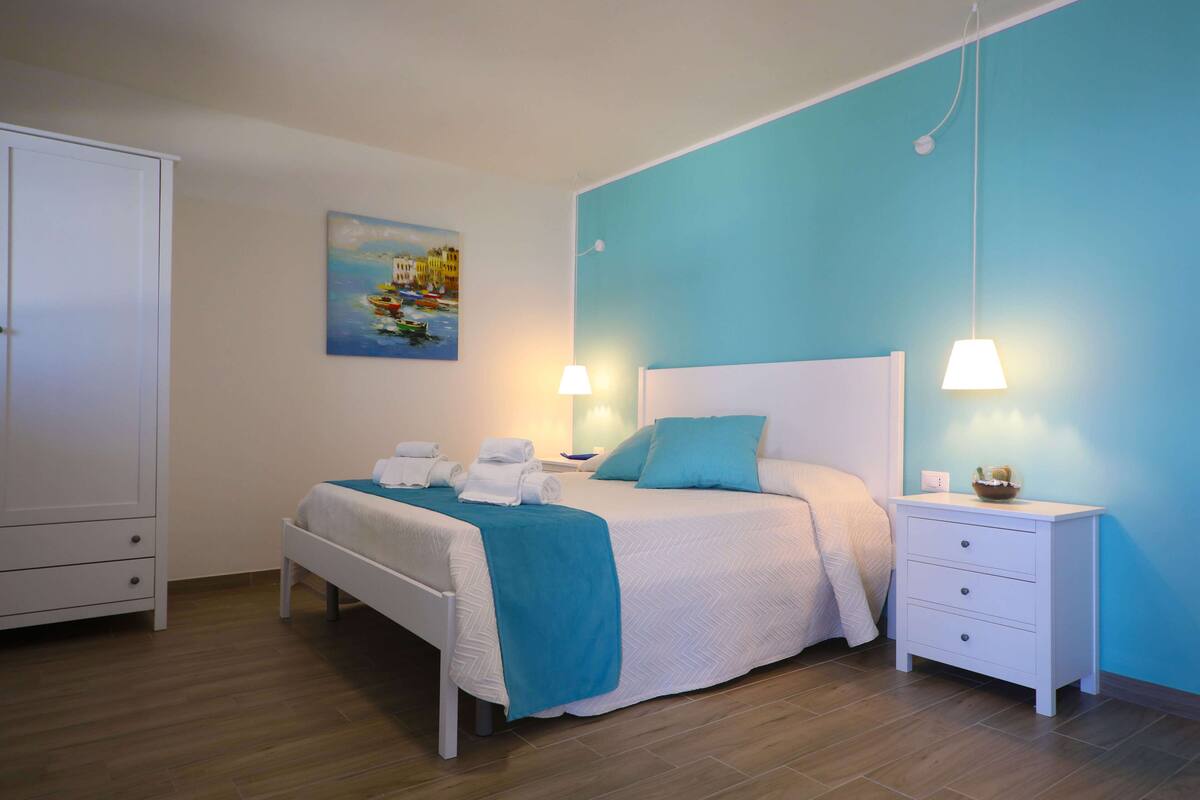 A bedroom with a bed, nightstands, a wardrobe, and a painting on the wall.