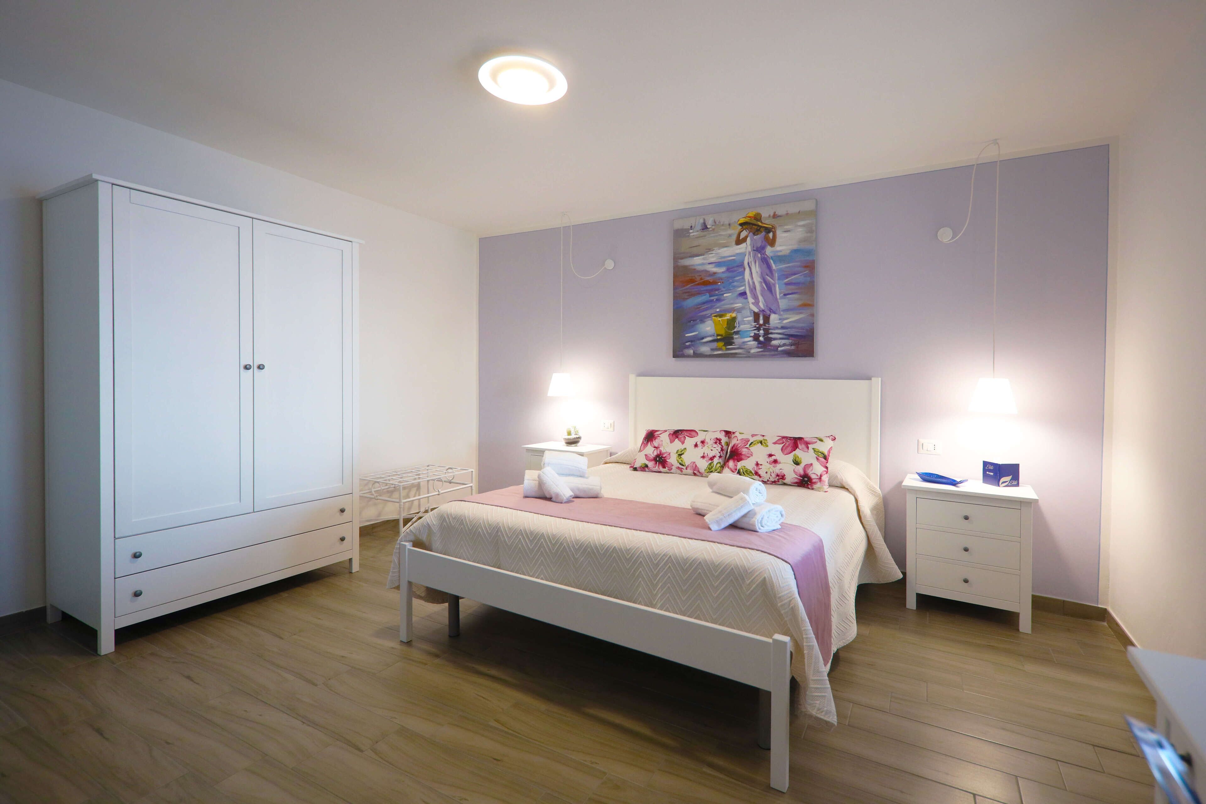 A bedroom with a bed, a nightstand, a wardrobe, and a painting on the wall.