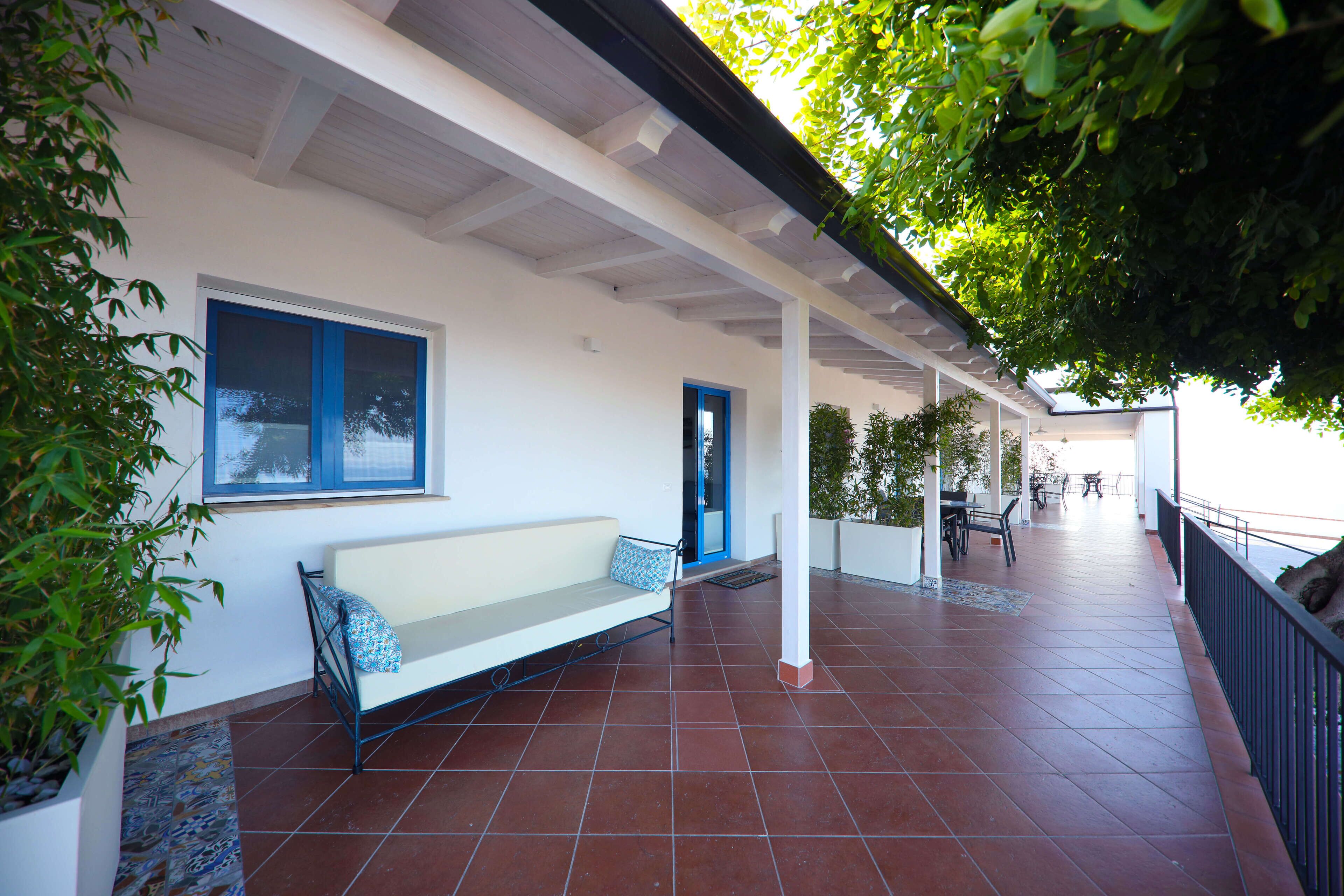 Un espacio al aire libre cubierto con un banco blanco, una puerta y vista al mar.