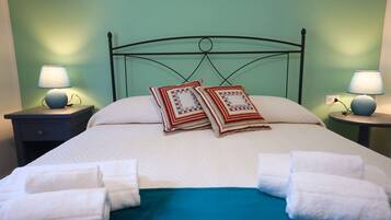 A neatly made bed with white linens and two decorative pillows, flanked by two bedside tables with lamps, in a room with green walls.