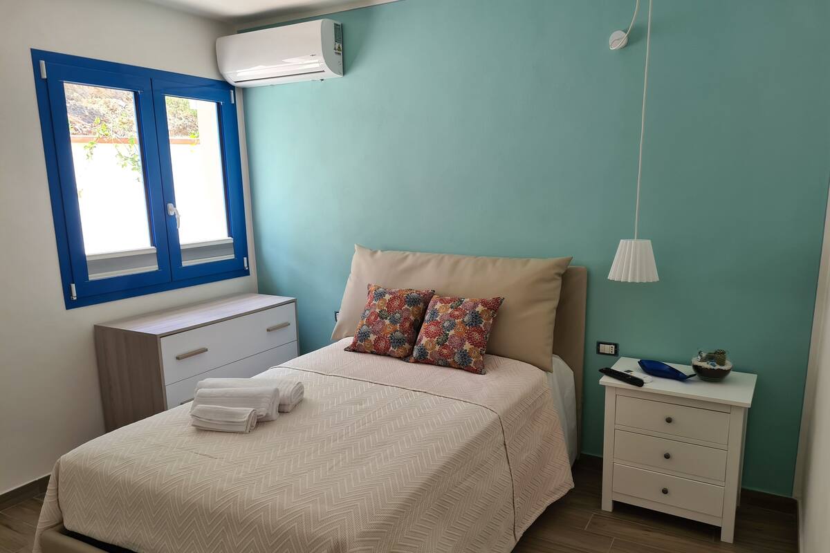 A bedroom with a bed, bedside tables, a window, and an air conditioning unit.