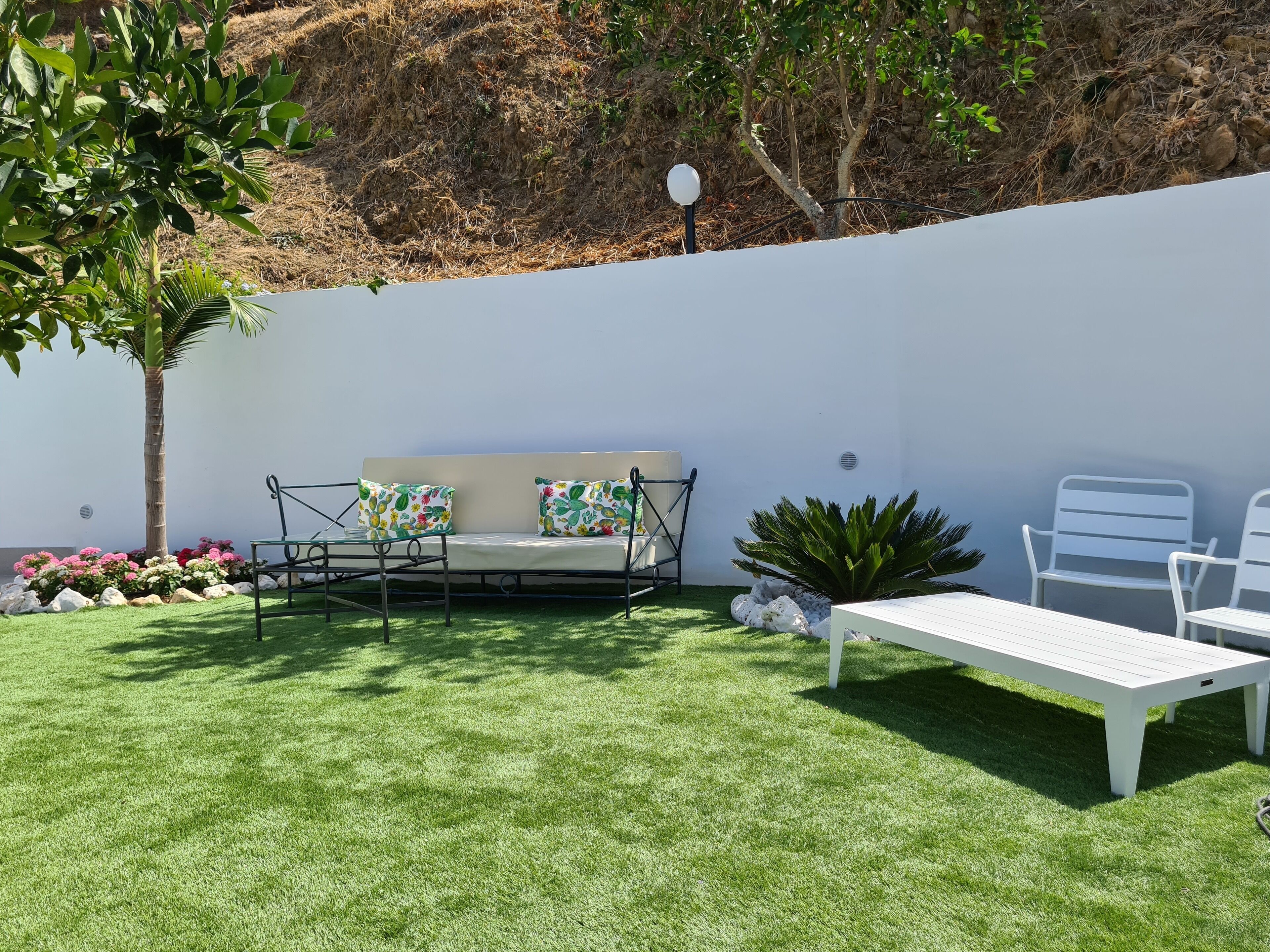 A patio area with a white sofa, two white chairs, a small table, and a lamp post.