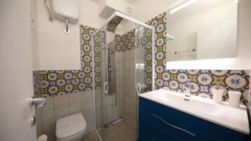 A bathroom with a toilet, a shower with glass doors, a sink, and a mirror.