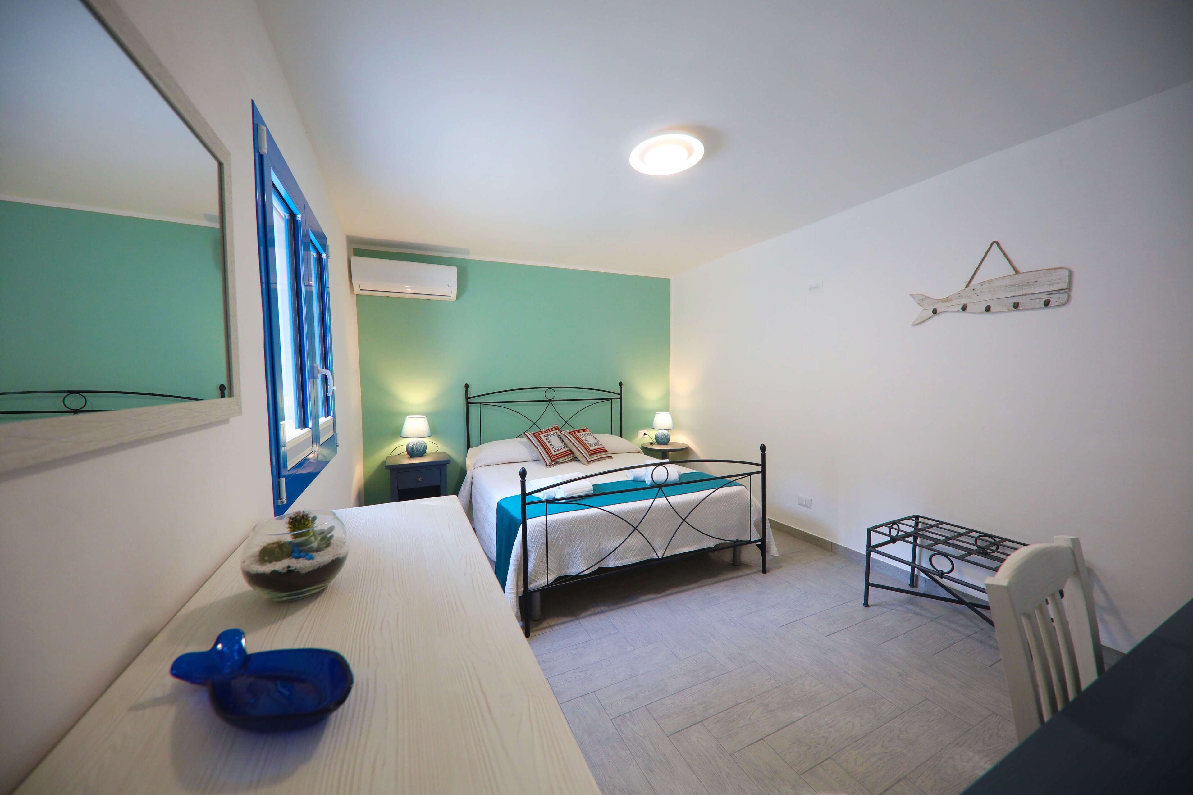 A bedroom with a bed, bedside tables, a chair, a dresser, a mirror, and a wall-mounted shelf.