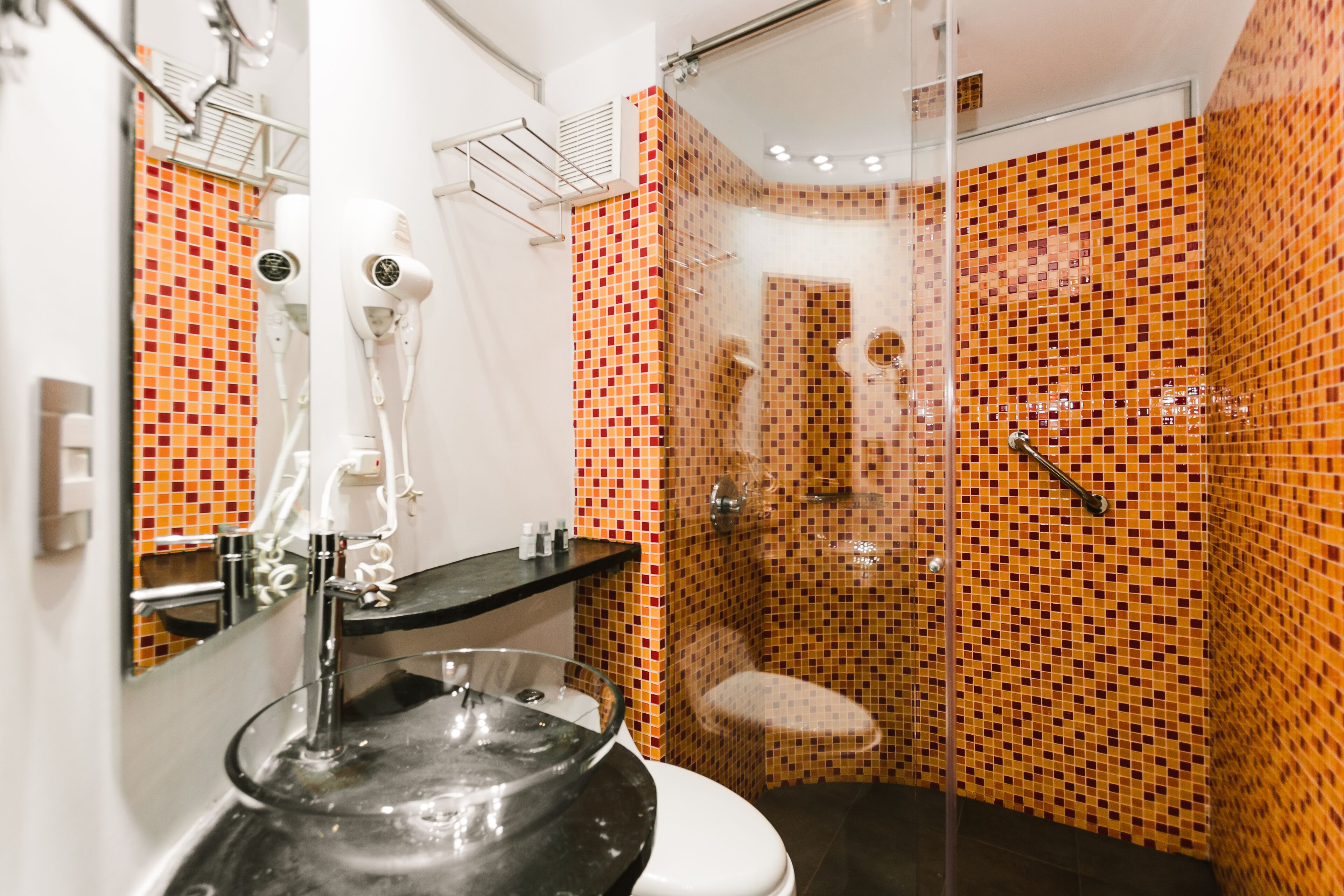Un bagno moderno con doccia vetrata, lavabo nero con lavagna in vetro e water bianco.