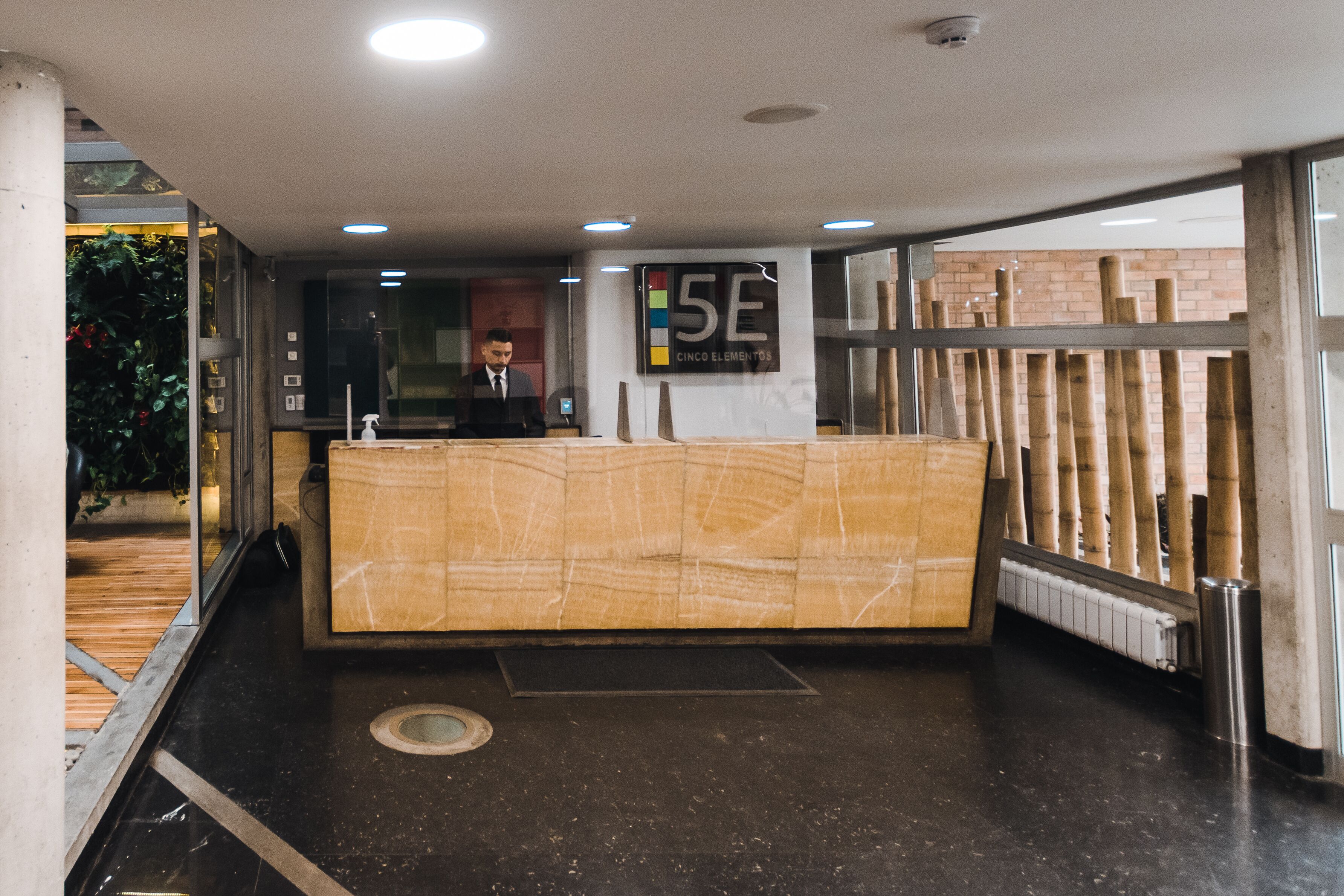 Uma receção com uma placa a indicar "5E Cinco Elementos" num hall moderno com parede de vidro e chão de madeira.