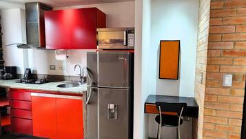 Una cocina compacta con armarios rojos, un refrigerador de acero inoxidable y un pequeño comedor con una silla negra.