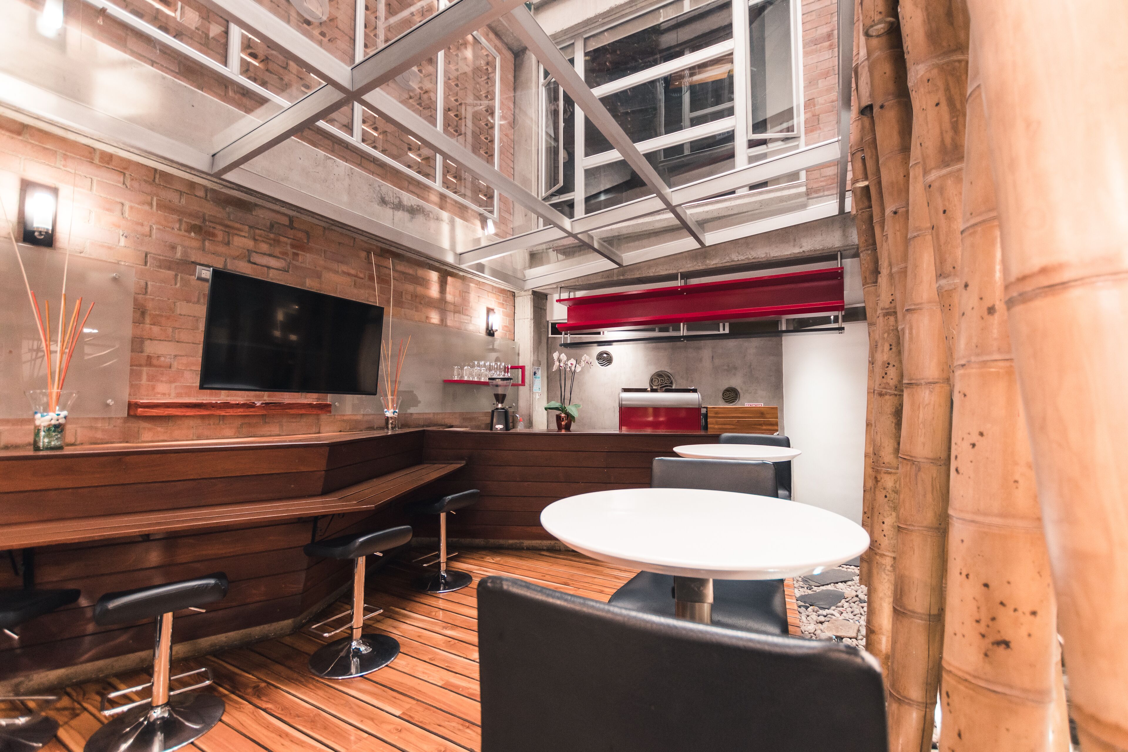 A modern bar area with wooden flooring, bar stools, a white round table, and a TV mounted on the wall.