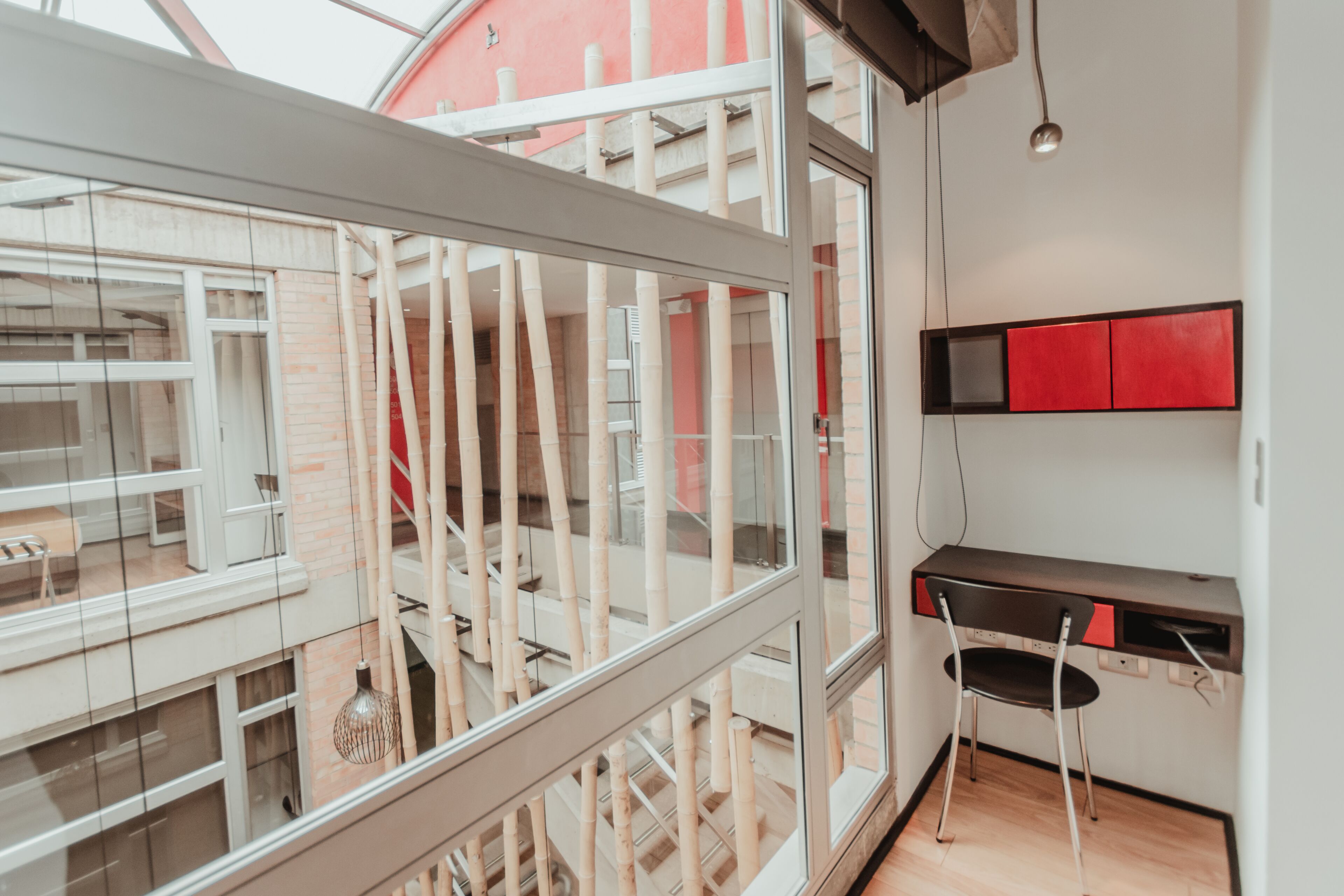Un interior moderno con un balcón de cristal, un escritorio con una silla y un armario rojo.
