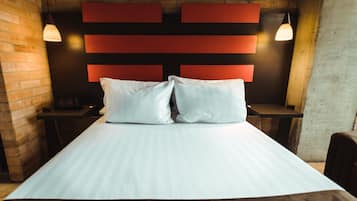 A hotel room with a bed, a brick wall, a red headboard, and two pendant lights.