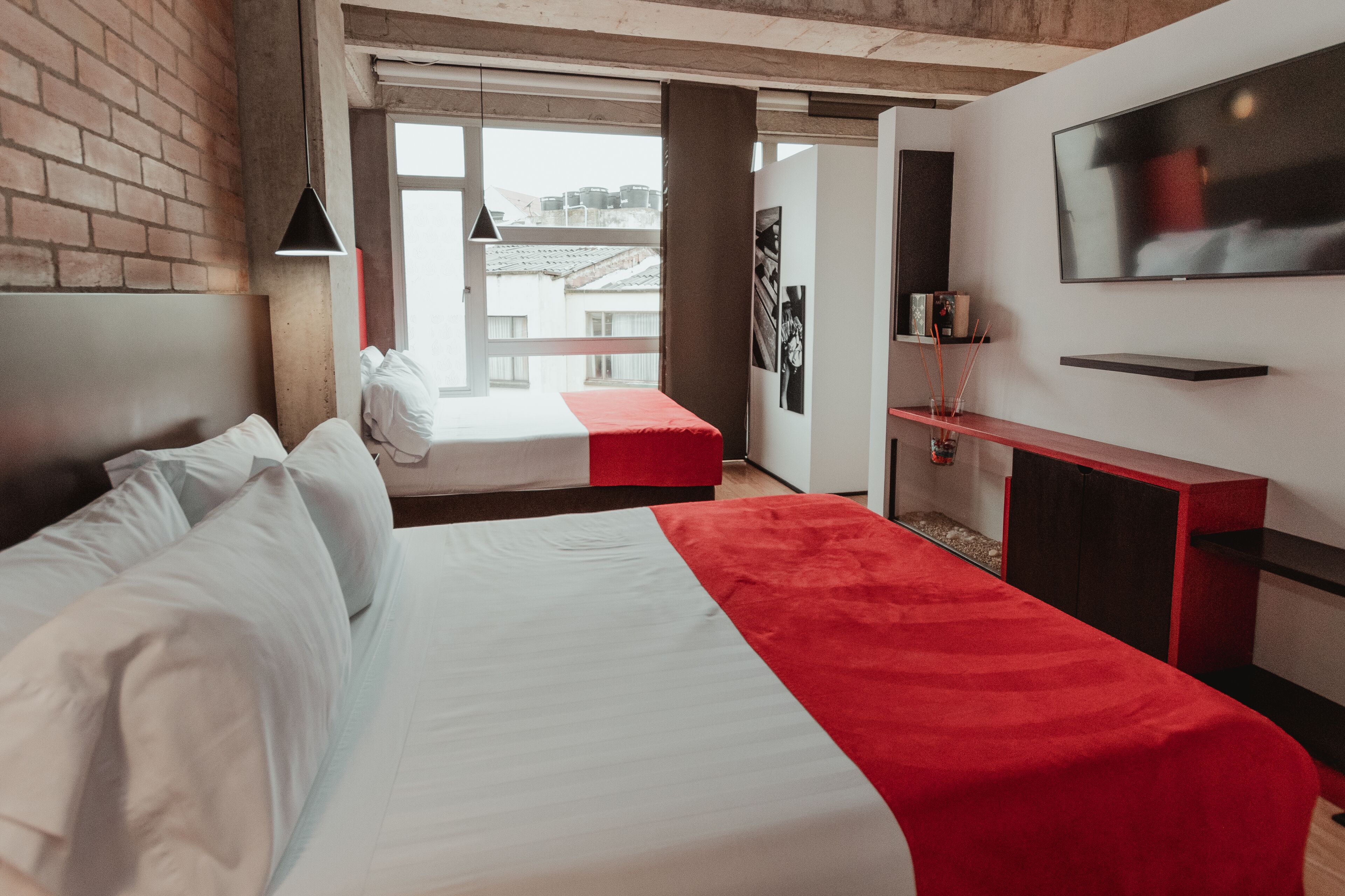 A hotel room with a large bed, a TV, a desk, and a window with a view of buildings.