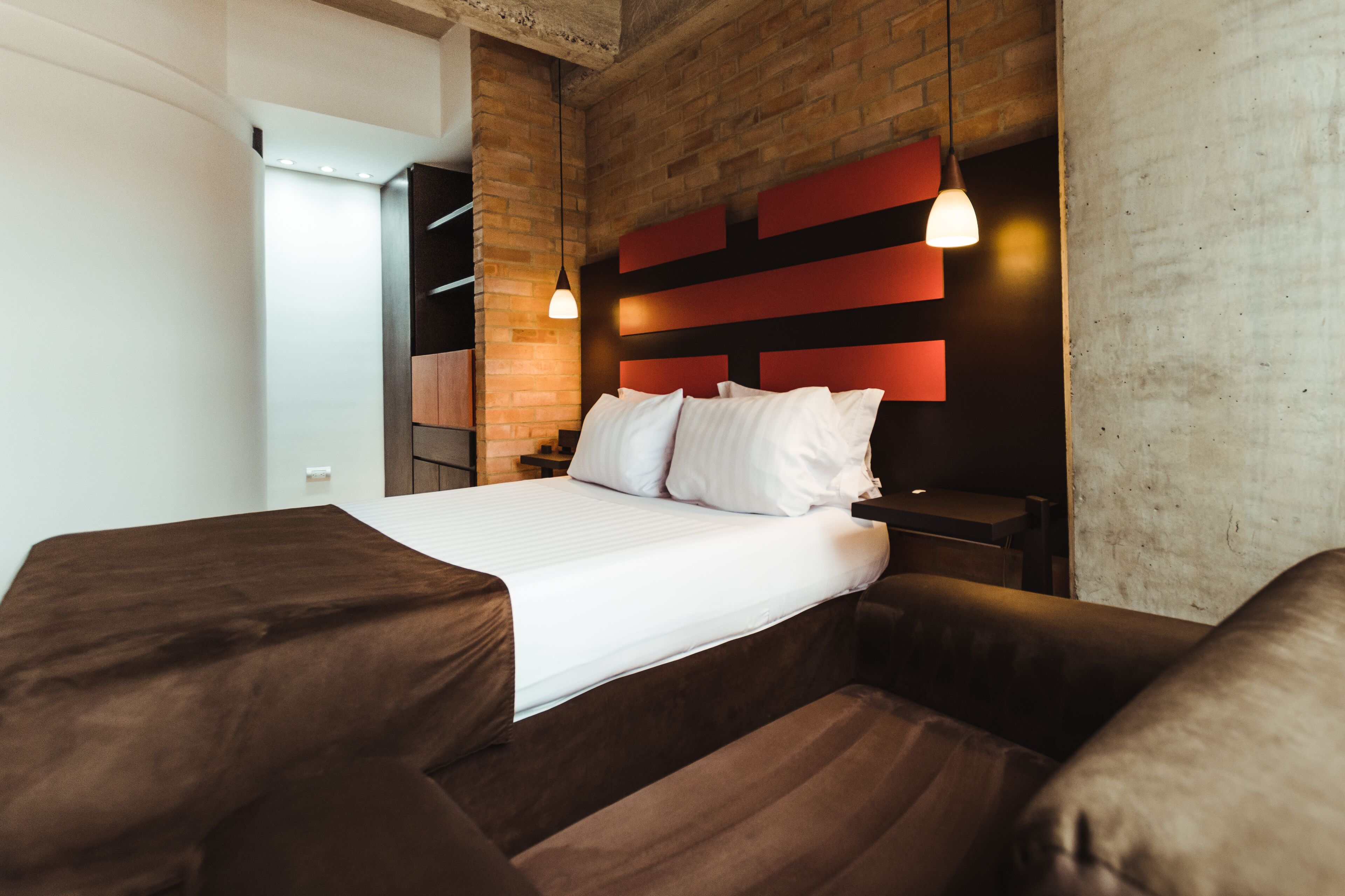 Une chambre d’hôtel moderne avec un grand lit, une tête de lit en bois et un mur décoratif en briques.