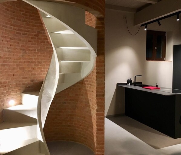 A modern kitchen with a curved staircase against a brick wall.