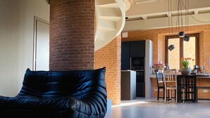 Una sala de estar moderna con un sofá de cuero negro, un pilar de ladrillo y una cocina al fondo.