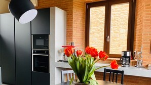 Una cocina moderna con un refrigerador, horno y cafetera negros. Hay un florero con flores rojas sobre una mesa de madera.
