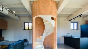 Un interior moderno con una escalera de caracol, un sofá de cuero negro y una zona de cocina.