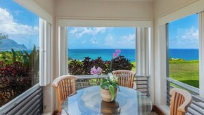 Una habitación con una mesa de vidrio, sillas, vistas al océano y plantas tropicales.