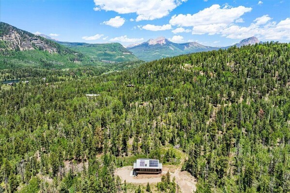 Una cabaña aislada rodeada de un bosque denso y montañas.